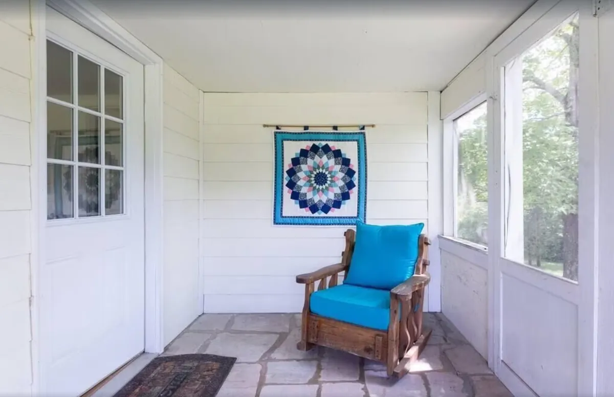 Featuring a cozy blue chair, quilted wall art, and stone flooring, this nook receives ample natural light, suggesting a tranquil space to relax, read, or enjoy the mountain ambiance. The elements evoke a rustic, resort-like charm befitting a mountain retreat, and the room's orientation hints at views beyond its walls.