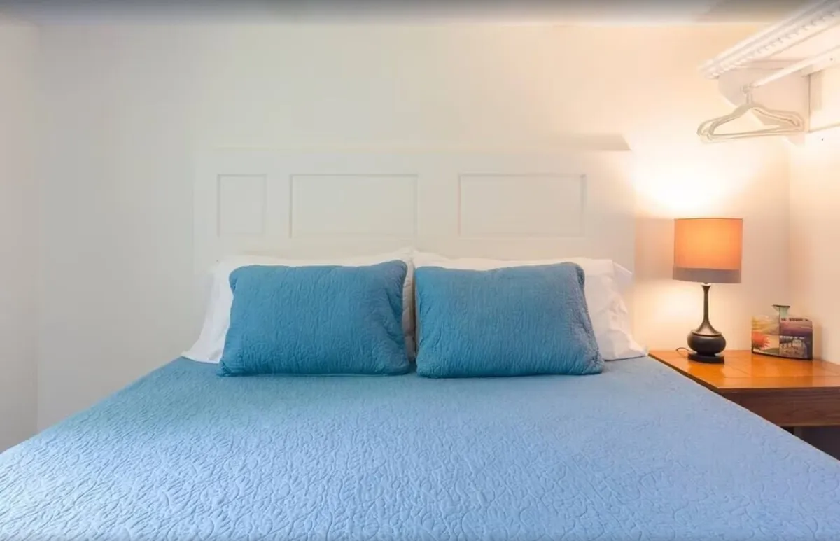 A cozy bedroom featuring a comfortable bed with blue bedding, a warm-lit table lamp, and a nightstand. The room exudes serenity and is designed for restful relaxation, perfect for recharging after a day of activities.