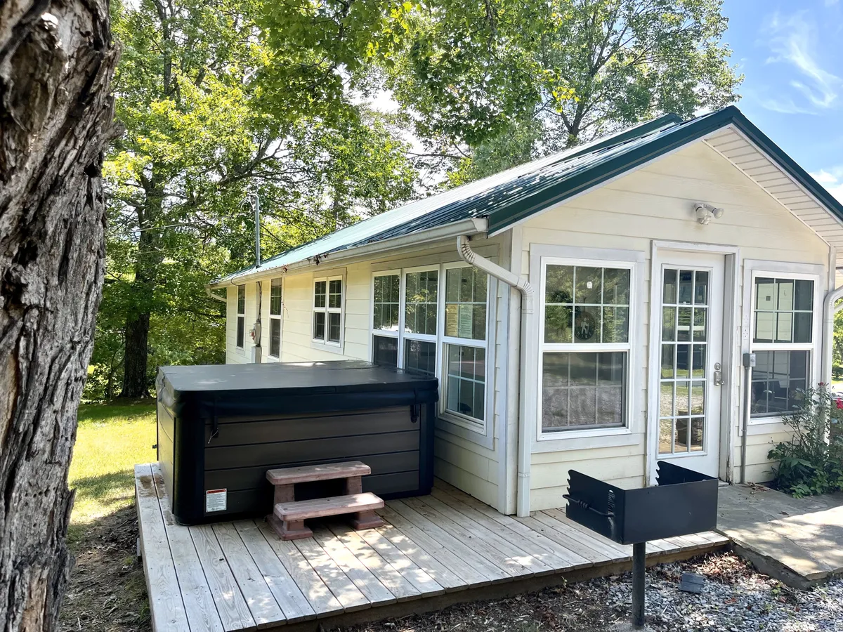 An exterior view showcasing the bubbling hot tub on a wooden deck, set against large house windows and rustic exterior walls. The space is designed for relaxation, with mountain vistas visible from the tub, and the deck is ideal for gatherings or stargazing at dusk.