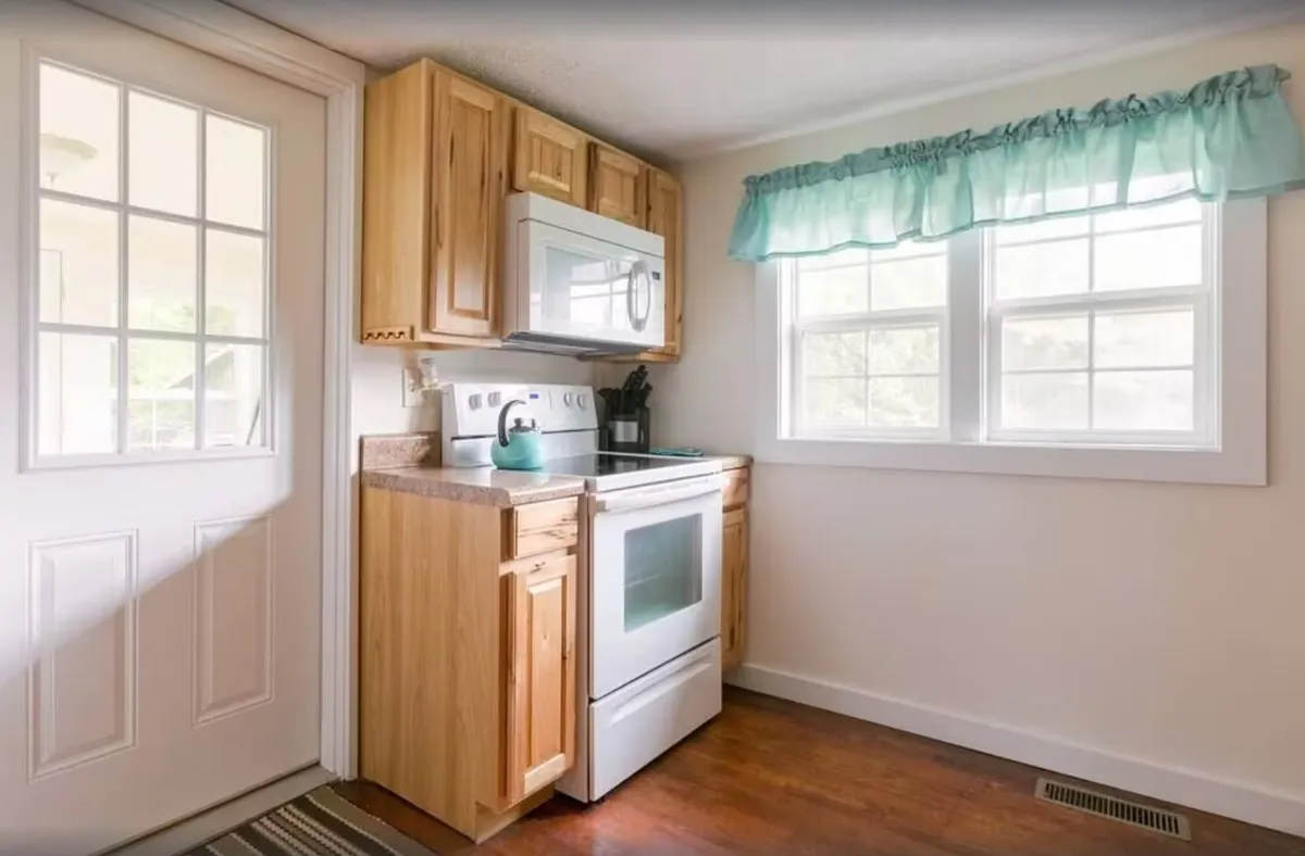 A kitchen with modern appliances, wooden cabinetry, and a window letting in sunlight, ideal for cooking family recipes or gathering together. The natural light and cozy mood create a welcoming atmosphere for memorable moments.