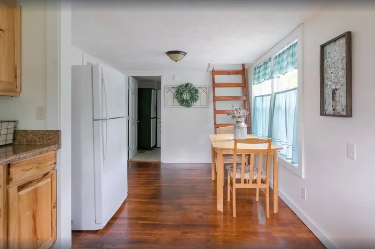 This image shows a cozy dining area with a wooden table set for a meal. A ladder leads to a loft area, and the kitchen appliances are visible in the background. Natural light pours in from nearby windows, creating a warm, inviting atmosphere perfect for group gatherings and shared meals.