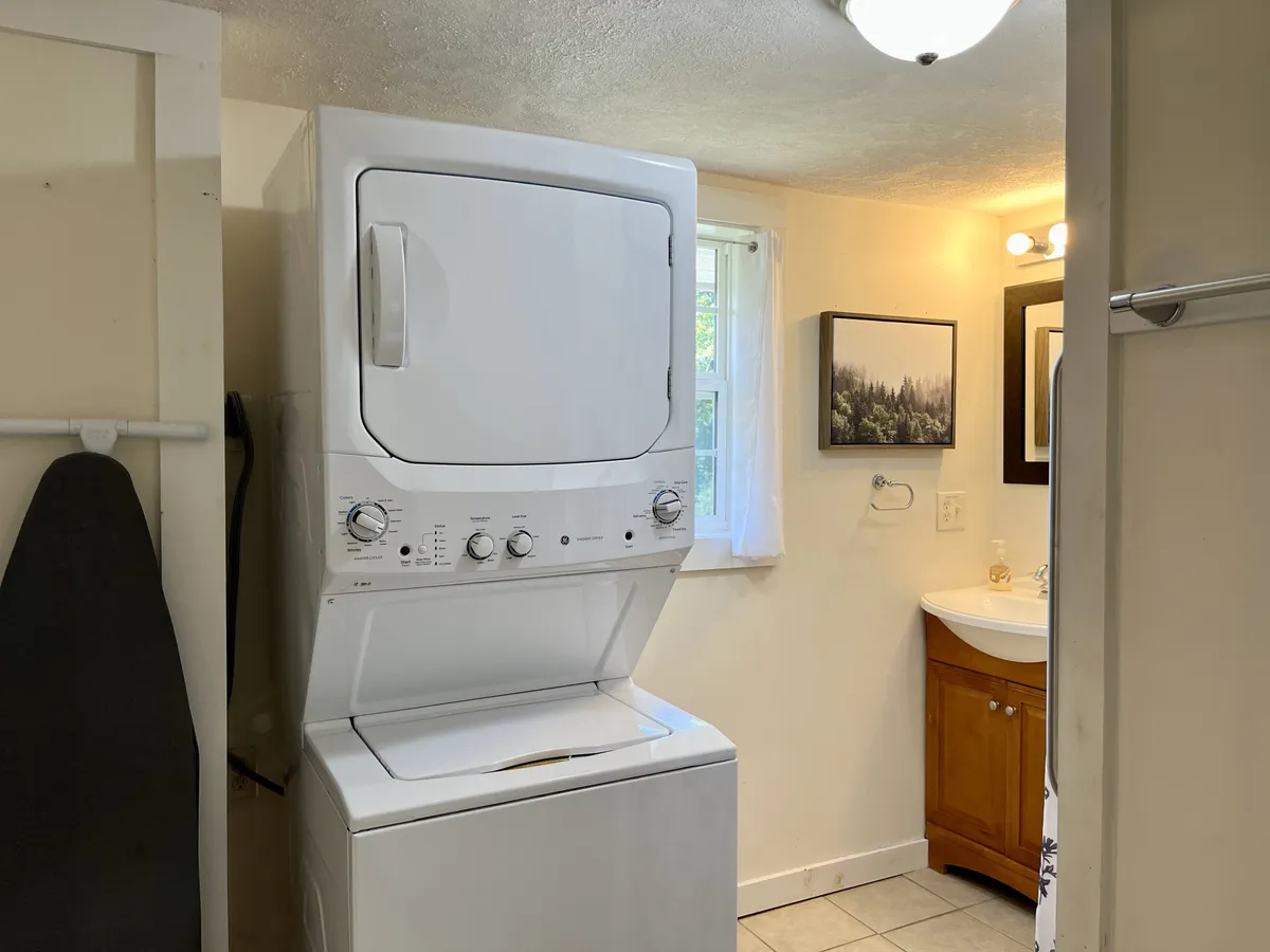 A practical laundry nook with a stacked washer and dryer, a sink with a storage cabinet, and framed wall art, making everyday routines convenient and accessible within the home.